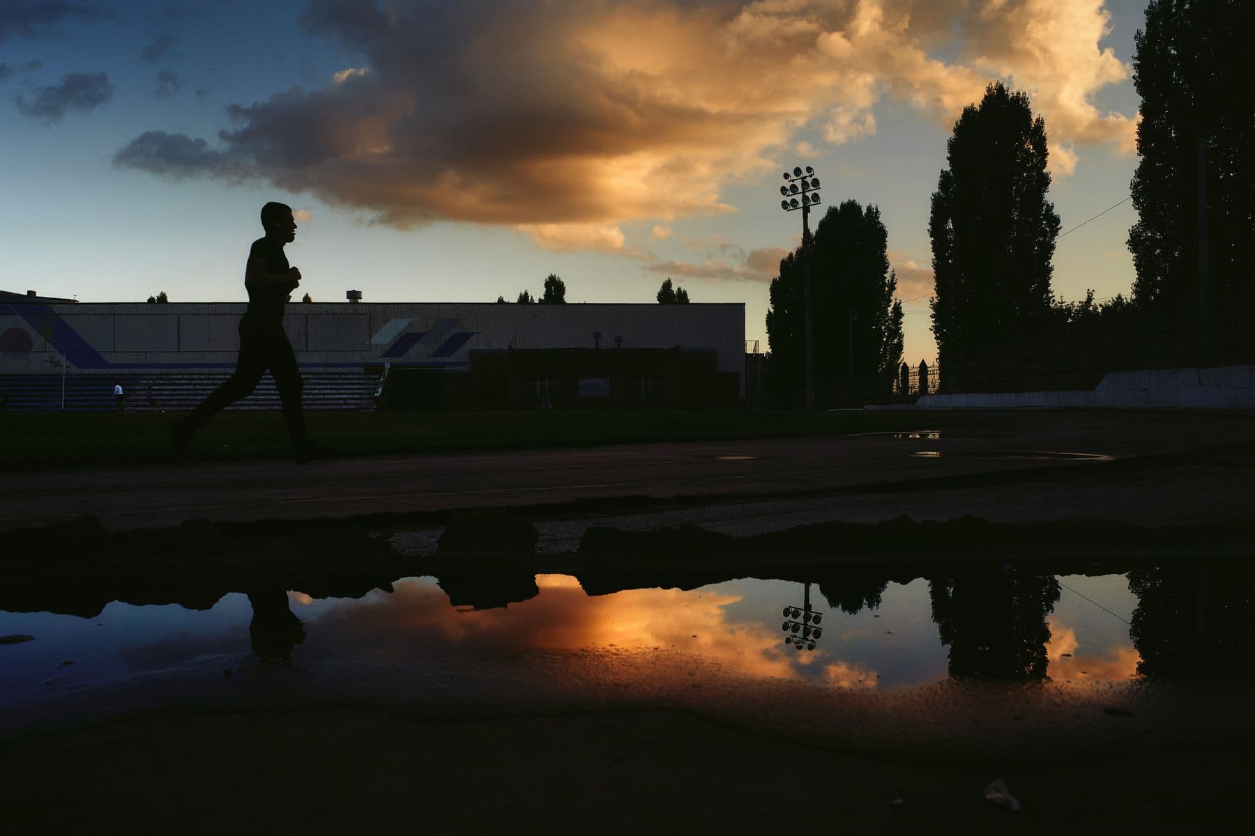 A runner's silhouette on an outdoor track against a low, dramatic sky